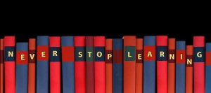 A row of books with colorful spines, arranged in a lateral transfer such that the titles on the spines spell out "NEVER STOP LEARNING" against a black background.