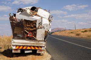 A small truck overloaded with various pieces of scrap metal and discarded appliances parked on the side of a rural road. The sky is partly cloudy, and there is dry grass along the road. In the background, there's a mountainous landscape, creating a stark contrast to the digital efficiency of Office 365.