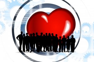 Silhouette of several people standing in front of a large, shiny red heart encircled by a partially visible black ring. The background features light blue gears and cogs, creating a mechanical contrast to the heart symbol, representing the healthiest balance between emotion and machine.