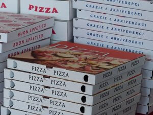 Stacks of pizza boxes are arranged, the front boxes prominently displaying the word "PIZZA" with images of pizzas on them. Some of the side boxes include Italian phrases like "BUON APPETITO" and "GRAZIE E ARRIVEDERCI," showcasing a rich Italian culture.