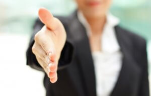 A person in a black suit extends their hand forward, offering a handshake. The background is blurred, shifting the focus to the inviting gesture—a classic move among employers initiating a greeting or sealing an agreement.