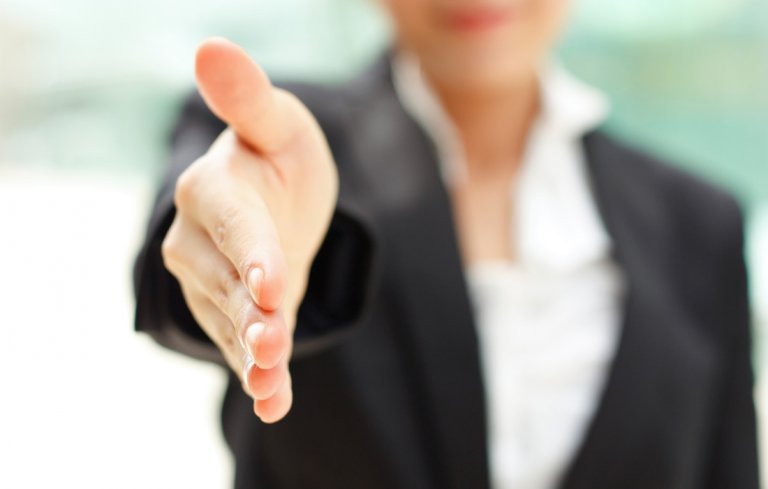 A person in a black suit extends their hand forward, offering a handshake. The background is blurred, shifting the focus to the inviting gesture—a classic move among employers initiating a greeting or sealing an agreement.