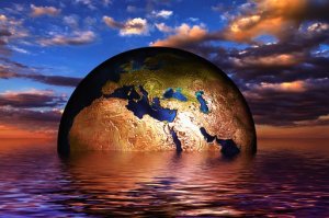 A digital art image depicting a globe with detailed landmasses and bodies of water, emerging from a reflective, calm ocean at sunset. The sky features scattered clouds with golden and orange hues, creating an atmosphere that feels like a work of art.
