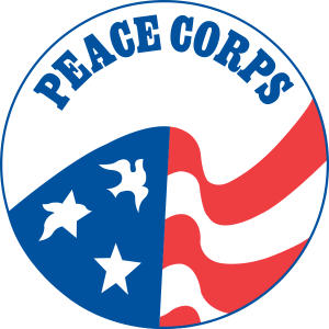 The image is the Peace Corps logo, a circular emblem with the left half displaying white stars and doves on a blue background, and the right half with curved red and white stripes. The words "PEACE CORPS," reflecting its federal government roots, are prominently displayed at the top.
