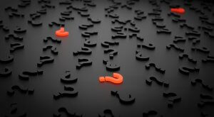 A dark surface is scattered with numerous black question mark symbols. Among them, a few question marks are highlighted in bright orange, standing out prominently from the rest—much like millennials disrupting conventional norms with their bold ideas.