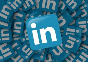 Blue LinkedIn logos with white "in" letters are scattered densely, resembling a student's desk covered in homework, with one prominent logo in clear focus at the center.