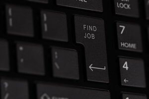 Close-up photo of a keyboard with a key labeled "FIND JOB" instead of the usual "Enter" or "Return" key. The keyboard, featuring black keys with white lettering, is slightly out of focus in some areas, highlighting the importance of crafting a standout cover letter.