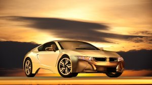 A sleek, golden sports car, an electric vehicle, is parked against a dramatic sunset sky. The car features modern, aerodynamic design with sharp lines and is positioned on a reflective surface, enhancing its glossy finish. The ambiance exudes luxury and sophistication.
