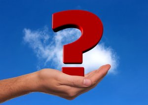 A hand is seen palm up, holding a large red question mark against a clear blue sky with a few scattered white clouds. The image suggests curiosity or questioning expectations.
