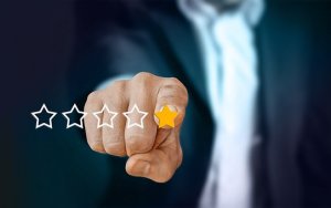 A hand in a suit pointing at a row of five stars, selecting the first star, which is colored gold. The other four stars are outlined in white. The background is dark and blurred, emphasizing employee engagement through the focused attention on the hand and stars.