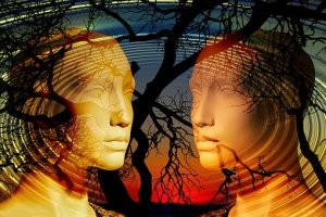 Two abstract human faces made of smooth, reflective material face each other against a vibrant, swirling background of concentric circles, tree branches, and a colorful sunset. The emotional scene blends nature with digital artistry.
