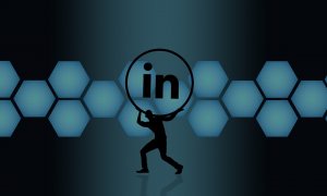 A silhouette of a person is lifting a large LinkedIn logo in front of a background composed of interconnected blue hexagons on a dark gradient backdrop, emphasizing the power of networking.
