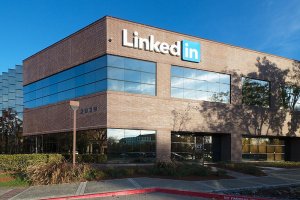 A modern, two-story brick building with large reflective windows and a prominently displayed "LinkedIn" sign graces the upper part of the facade. The surrounding area features landscaped greenery and a clear blue sky.
