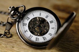 A vintage silver pocket watch with an open lid lies on a wooden surface, akin to a well-crafted cover letter. It features Roman numerals on the outer edge, and the inner workings of the mechanism are visible through a transparent center. The chain is partially visible on the left.