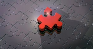 A glossy black jigsaw puzzle with a single piece missing near the center. The missing piece, which is red and slightly elevated above the rest, casts a small shadow—much like a standout individual in a workforce—highlighting its unique color and placement against the otherwise uniform puzzle.