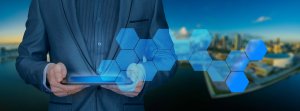 A person in a suit holds a tablet with one hand and touches a virtual interface with hexagonal patterns using the other, illustrating information governance. The background shows a cityscape with buildings and a body of water under a clear blue sky.