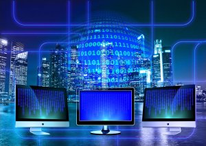 Three computer monitors displaying blue digital binary code are set against the backdrop of a modern cityscape illuminated with blue lights. The scene includes a large glowing globe with binary code overlay, emphasizing themes of technology, connectivity, and the world of programming.