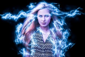 A woman with long, flowing hair stands confidently, surrounded by bright blue electric energy arcs emanating from her superpowers. She is wearing a patterned dress, and the dark background makes the electric energy appear vibrant and dynamic. The image has a powerful and mystical vibe.