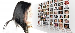 A woman with long dark hair is resting her chin on her hand, looking at a white wall filled with a grid of small portraits featuring various people, perhaps even your boss. The arrangement of the portraits creates a 3D effect, making it seem like the wall extends into the distance.