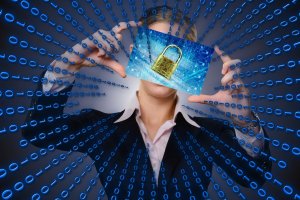 Person in a business suit holding a transparent screen displaying a digital padlock in front of their face. The background consists of blue binary code extending in a radial pattern, symbolizing cybersecurity, online privacy, and data protection.
