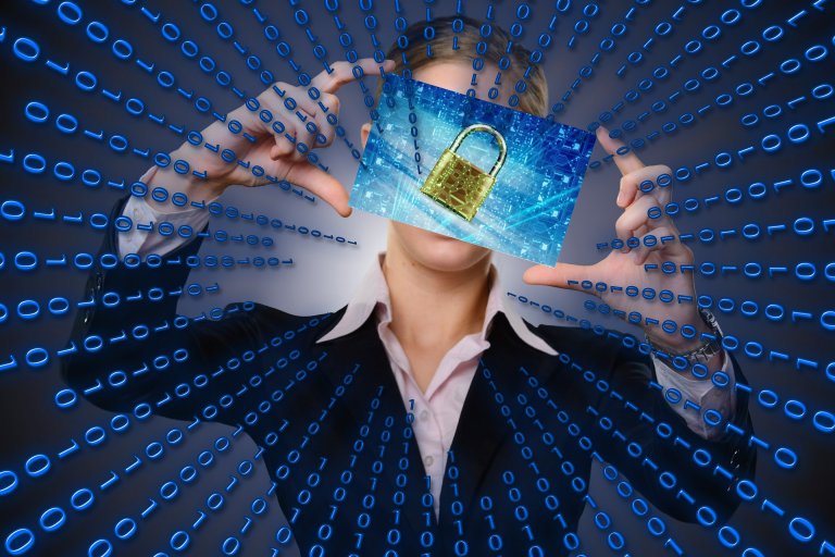 Person in a business suit holding a transparent screen displaying a digital padlock in front of their face. The background consists of blue binary code extending in a radial pattern, symbolizing cybersecurity, online privacy, and data protection.