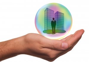 A hand is shown holding a transparent, colorful bubble with two tall buildings and a person in a suit inside, symbolizing the safeguarding of business or professional interests, including workers' compensation. The background is white.