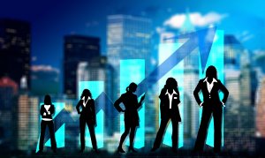 Silhouettes of five businesswomen stand in front of a cityscape backdrop with blue bar graphs and an upward arrow, symbolizing leadership, growth, and success in business. The background features tall buildings and a mix of light and dark sky tones.