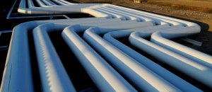 A network of large white industrial pipes arranged in parallel rows creates complex curves and turns. The pipes are situated outdoors, with the ground and a field visible in the background. As sunlight casts shadows, highlighting the pipes' contours, jobseekers may marvel at this engineering feat.