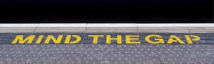 A subway or train platform edge with the words "MIND THE GAP" painted in bold yellow letters, serving as a crucial roadmap for passengers to be cautious of the space between the train and the platform.