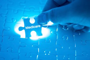 A hand is placing a glowing jigsaw puzzle piece labeled "Medicare" into the corresponding slot of a puzzle. The surrounding pieces, bathed in a blue hue, are visible but not yet connected.