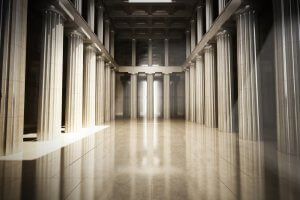A grand hall with tall, Greek-style marble columns and a polished, reflective floor. Natural light streams in from openings above, illuminating the columns and creating a majestic, serene atmosphere. Despite the challenges of COVID-19, its beauty remains untouched. The ceiling features intricate coffered detailing.