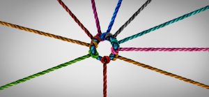 A circular knot formed by ten interwoven, multicolored ropes emerges from the center, each rope extending outward in a different direction. The background is a plain, light gray, emphasizing the vibrant colors and intricate connections of the ropes, symbolizing teamwork and unity.
