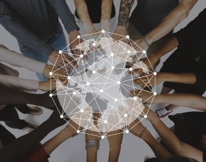 A circle of diverse hands reaching toward the center from various directions, with a network pattern of interconnected dots and lines overlaid on the image, suggesting unity, collaboration, and global networking.