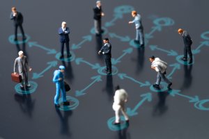 Miniature figurines representing various professionals standing apart on a network diagram with interconnected arrows, illustrating communication or social connections within a professional network.