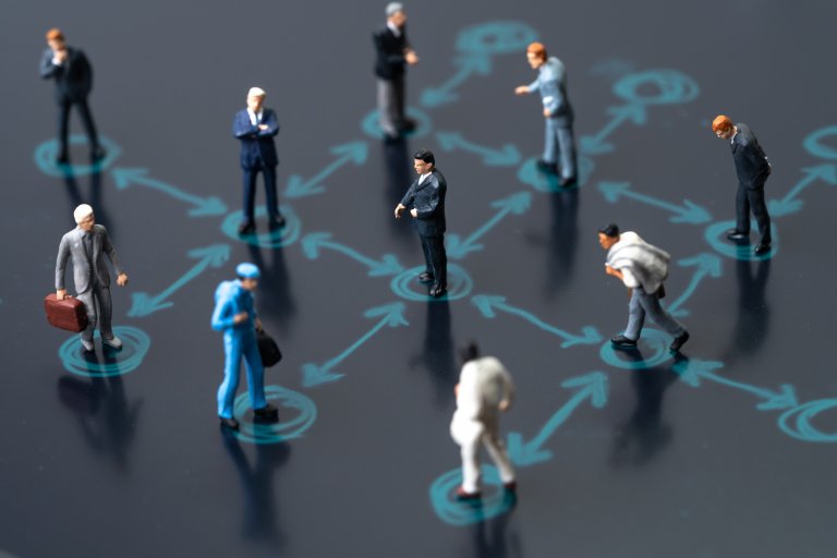 Miniature figurines representing various professionals standing apart on a network diagram with interconnected arrows, illustrating communication or social connections within a professional network.