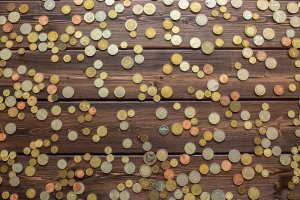 A variety of scattered coins of different sizes, colors, and denominations are spread out across a wooden surface. The coins include light and dark tones, representing various currencies and values. This scene symbolizes the diverse opportunities that jobseekers encounter on their journey.