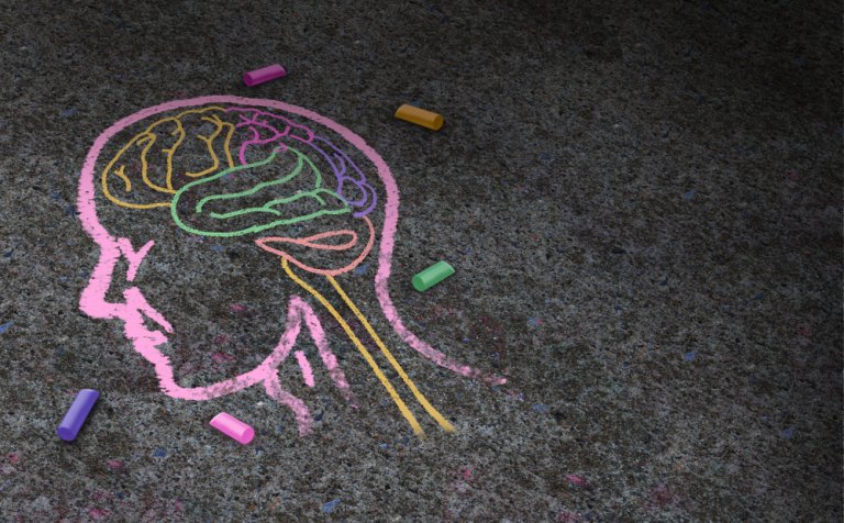 A chalk drawing on a textured surface depicts a profile of a human head and neck, with colorful outlines of the brain and spine, symbolizing mental health. Various colored chalk sticks are scattered around the drawing.
