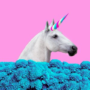 A white horse, adorned with a striped, blue and pink unicorn horn, stands among vibrant blue flowers against a bright pink background—a whimsical scene capturing the latest trends in magical realism.