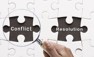 A hand holds a magnifying glass over a missing puzzle piece labeled "Conflict." Beside it, another elusive piece is marked "Resolution." The backdrop consists of neatly assembled white puzzle pieces.