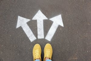 Yellow shoes standing at a junction with three painted white arrows on the asphalt, pointing left, right, and straight ahead, symbolizing choices in careers in government.