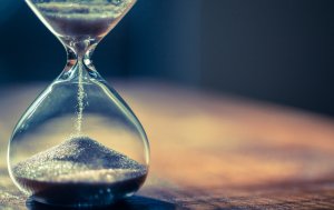Close-up of an hourglass with sand trickling down from the upper bulb to the lower bulb. The background is blurred with soft, warm lighting, giving a sense of calm and the passage of time, reminiscent of the steady progress in careers in government.