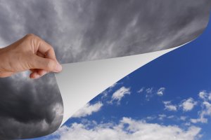 A hand is peeling back a layer of dark storm clouds to reveal a bright, clear blue sky with white, fluffy clouds underneath. This imagery symbolizes not only the transition from bad weather to good weather but also the promising horizons available through careers in government.