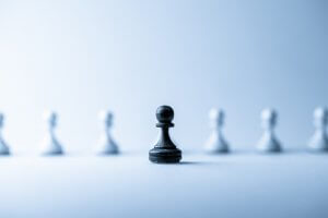 A single black pawn chess piece is positioned in the center of the frame, standing out against a blurred line of white pawn pieces in the background. The scene, reminiscent of navigating careers in government, is lit with a soft blue hue, giving it a cool, serene ambiance.