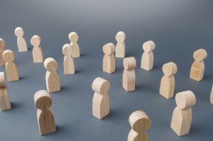 Wooden human-like figures are scattered across a gray surface, varying in orientation and spacing. The simplistic shapes suggest abstract representations of people, creating a feeling of social interaction or community dynamics, much like the intricate network found in careers in government.