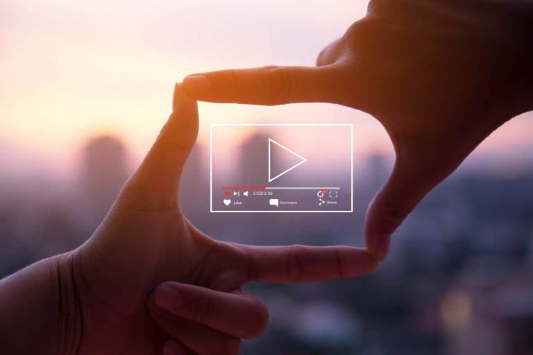 Two hands create a frame around the silhouette of a cityscape at sunset. A play button and video interface icons (like, comment, share) are superimposed on the view, suggesting the scene is being captured for a video about government jobs.