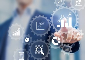 A person in a suit is interacting with a transparent screen displaying various data analytics icons, including graphs, charts, and binary code within gear symbols. The image represents data analysis and business intelligence concepts vital for careers in government.
