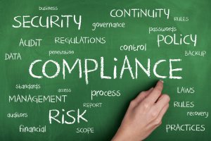 A person's hand writing the word "COMPLIANCE" in large letters on a green chalkboard, surrounded by other related terms in various sizes, such as "SECURITY," "RISK," "POLICY," "DATA," "AUDIT," "MANAGEMENT," and "REGULATIONS." The scene mirrors the meticulous planning often seen in careers in government jobs.