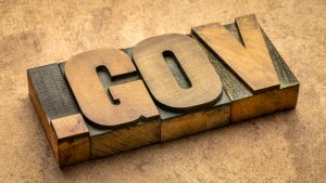 The word "GOV" is displayed in large, vintage-style wooden block letters on a textured brown surface, evoking thoughts of stability amidst the challenges brought by Covid-19.