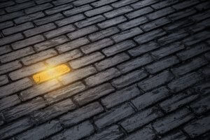 A close-up view of a cobblestone pavement with a single yellow brick glowing among the gray and dark stones. The glowing brick stands out, much like exceptional employee performance shines amidst routine tasks, creating a striking contrast with the surrounding dim and weathered cobblestones.