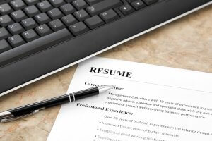 A close-up of a printed resume on a desk with a pen placed on top of it. The edge of a computer keyboard is visible in the top left corner. The resume meticulously lists sections such as Career Objective and Professional Experience.